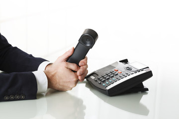 Close up of businessman hands dialing out on a black deskphone - obrazy, fototapety, plakaty