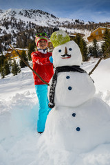Winter fun, happy girl playing with snowman with a mustache