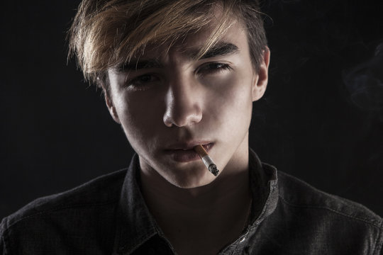portrait of a young handsome man smoking a cigarette on black ba