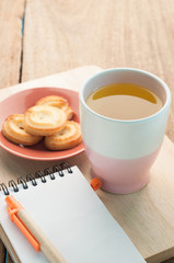 Tea cup, dessert cookie on wood floor and notepad paper.