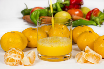 Squirt of tangerine orange juice falls into a glass, forming bubbles and splashes. Different vegetables at background