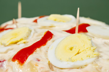 Detail of eggs and red pepper decorating an Olivier salad (also known as Russian salad), covered by mayonnaise