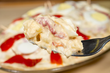 Close-up of fork with Olivier salad (Russian salad), with a tray of this kind of salad at background