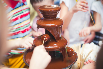 Vibrant Picture of Chocolate Fountain Fontain on childen kids birthday party with a kids playing around and marshmallows and fruits dip dipping into fountain 