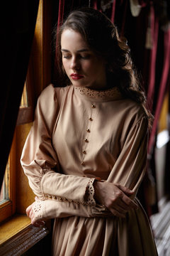 Young woman in beige vintage dress of early 20th century standin