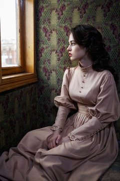 Young woman in beige vintage dress of early 20th century sitting