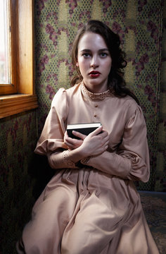Young woman in beige vintage dress of early 20th century sitting