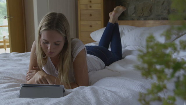 young woman lying on her bed using a digital tablet