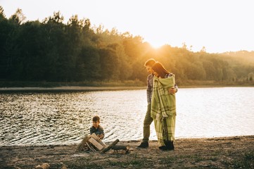 Happy young family sitting around the campfire on the beach at n