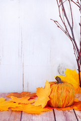 Decorative pumpkin, fall leaves and bare branches on wood table. Good for fall or Halloween