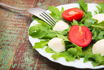 Green salad made with arugula, tomatoes, cheese mozzarella balls and sesame on plate
