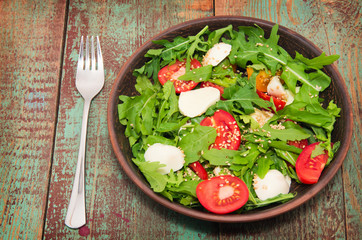 Green salad made with arugula, tomatoes, cheese mozzarella balls and sesame on plate
