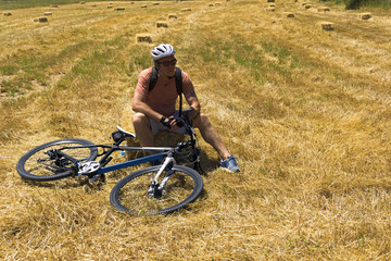 Cyclist man is resting on hay bale in a field