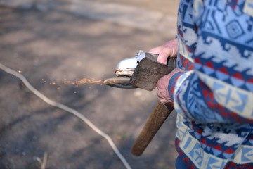 Close up of a man sharpen an ax using electric grinder. Sparks w