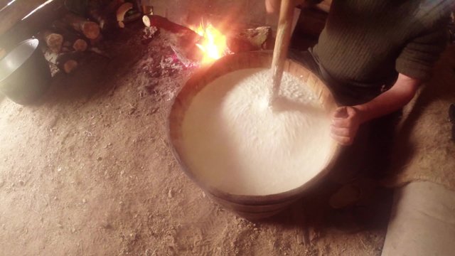 churning fermented sheep's milk wooden gadgets in a wooden barrel on the background of a bonfire