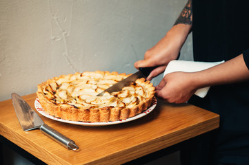 homemade delicious traditional apple pie with caramel on a plate on wood table and white background cool girl with tattoo slicing with knife trendy style