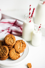 Oatmeal cookies with milk in jars on white wooden background