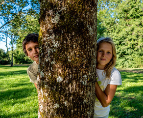Two children, boy and girl, coming out from behind a tree and watching us