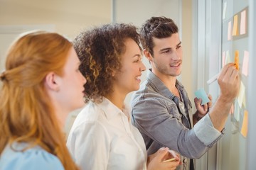 Businessman writing a post it while colleagues are looking at it