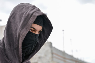 unrecognizable young man wearing black balaclava sitting on old