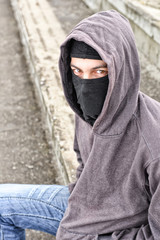 unrecognizable young man wearing black balaclava sitting on old