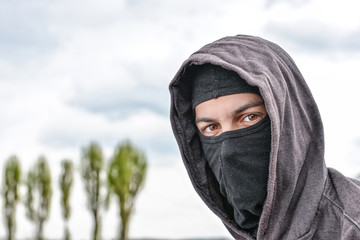 unrecognizable young man wearing black balaclava sitting on old