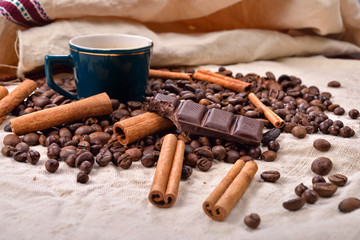 Cup of hot coffee with cinnamon sticks, bitten bar of chocolate