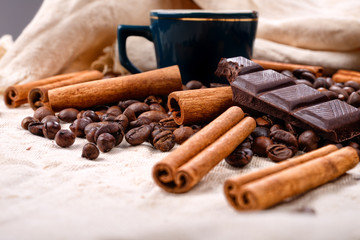 Cup of hot coffee with cinnamon sticks, bitten bar of chocolate