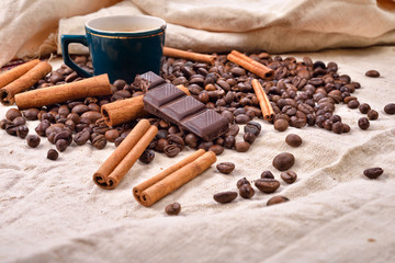 Cup of hot coffee with cinnamon sticks, bitten bar of chocolate