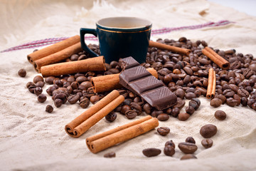 Cup of hot coffee with cinnamon sticks, bitten bar of chocolate