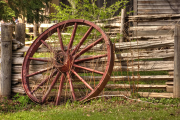 Fototapeta na wymiar A single rustic wagon wheel leaning against wooden fence.