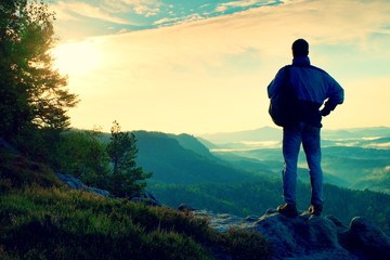 Fototapeta premium Silhouette of tourist with backpack. Sunny spring daybreak in rocky mountains. Hiker with sporty backpack stand on rocky view point above misty valley.