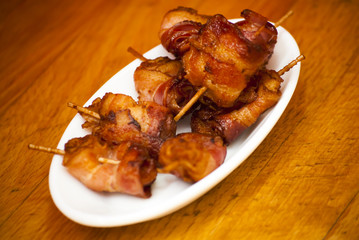 Rolls of slices of cooked bacon subject with a toothpick on a wh