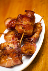 Rolls of slices of cooked bacon subject with a toothpick on a wh