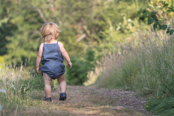 Baby girl with blue jeans costume walking away on path