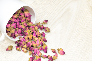 tea roses in a white cup scattered on the wooden table