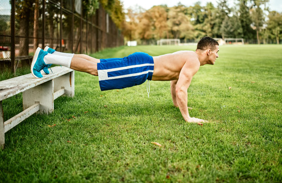 athletic built man doing pushups and core training in park. Fitness basketball player training on grass
