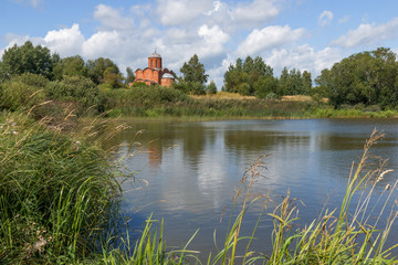 Fototapeta na wymiar Old orthodox church on the bank of a pond on a summer day. Church of the Savior on Kovalev on the outskirts of Veliky Novgorod