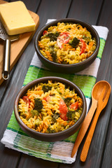 Baked tricolor fusilli pasta and vegetable (broccoli, tomato) casserole in rustic bowls, photographed with natural light (Selective Focus, Focus in middle of first dish)