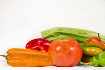 Red tomato beside carrots and other vegetables, such as  peppers and lettuces