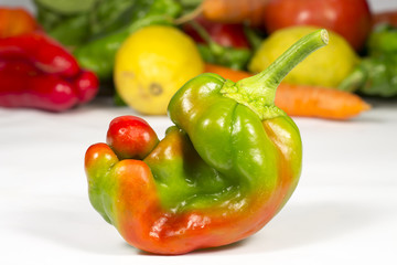 Small red and green pepper in front of other fruits and vegetables