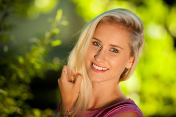 Beautiful young blonde woman resting on a bench at dusk in summer