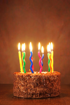 Birthday chocolate cake with many burning candles against brown background
