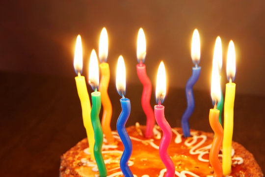 Burning candles on a birthday chocolate cake against brown background