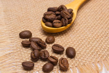 Heap of coffee beans with wooden spoon on jute canvas