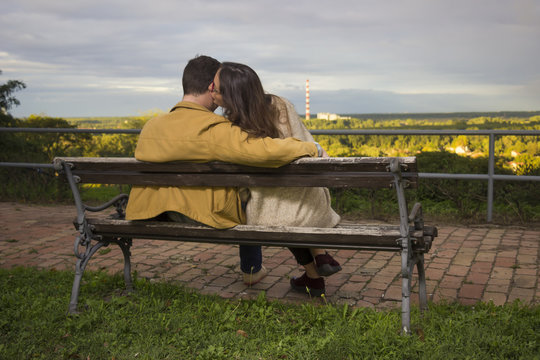 Young Couple Sitting On A Bench, Shot From Behind.