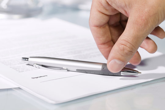 Close-up of a hand taking a pen to fill and sign documents.