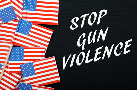 The words Stop Gun Violence in white text on a blackboard alongside miniature flags of the United States of America