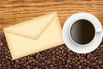 Close-up of roasted coffee beans and envelop and coffee cup over