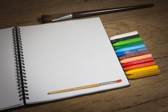 notebook and colorful crayons on wooden background.
